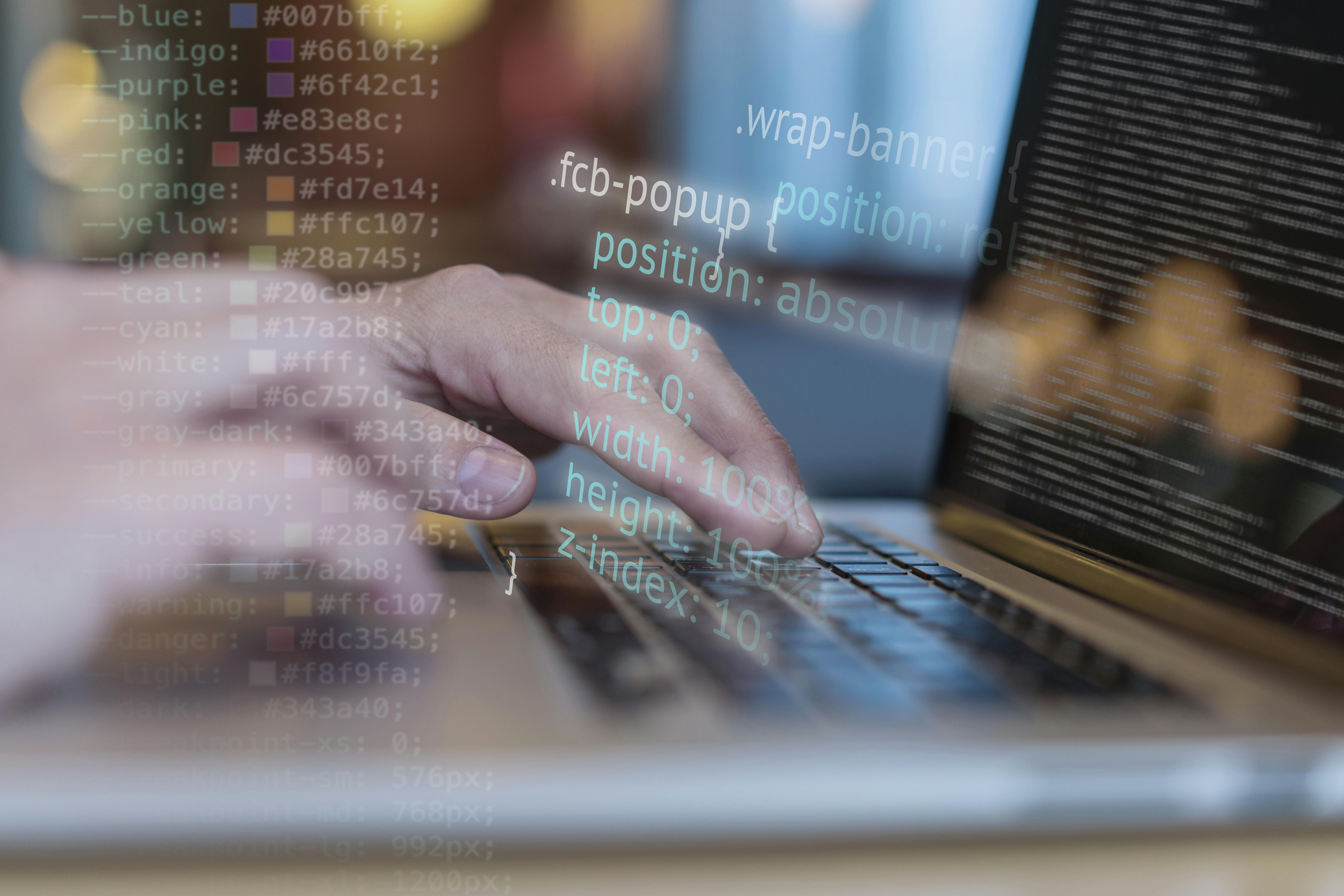 Wazig zijn te zien het toetsenbord van een laptop met twee handen. Het scherm staat vol programmeercode. Over de foto is programmeercode geplaatst.