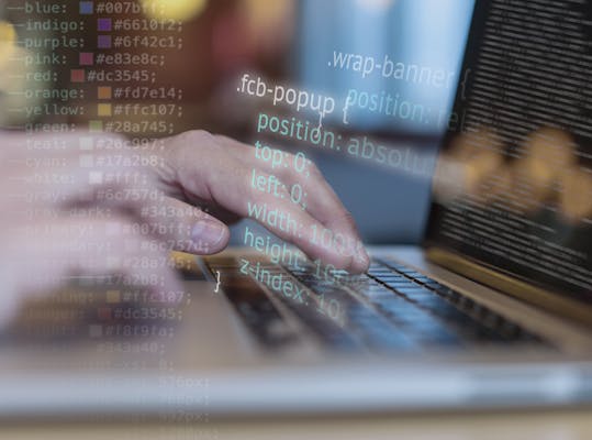 Wazig zijn te zien het toetsenbord van een laptop met twee handen. Het scherm staat vol programmeercode. Over de foto is programmeercode geplaatst.