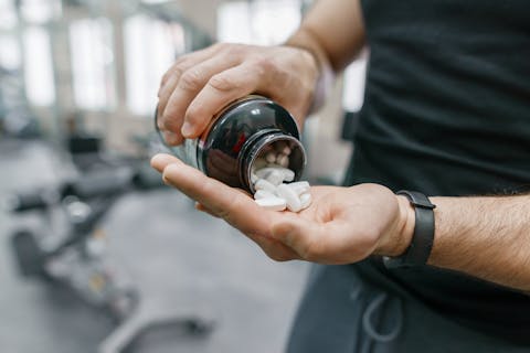 Man in een fitness-ruimte schudt witte pillen uit een potje Man in een fitness-ruimte schudt witte pillen uit een potje