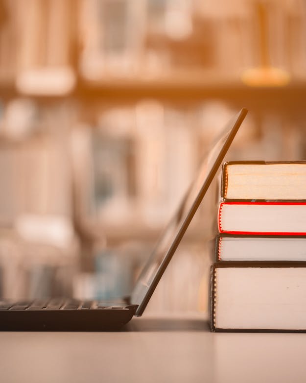 Een opengeklapte laptop leunt tegen een stapeltje boeken aan. Een opengeklapte laptop leunt tegen een stapeltje boeken aan.