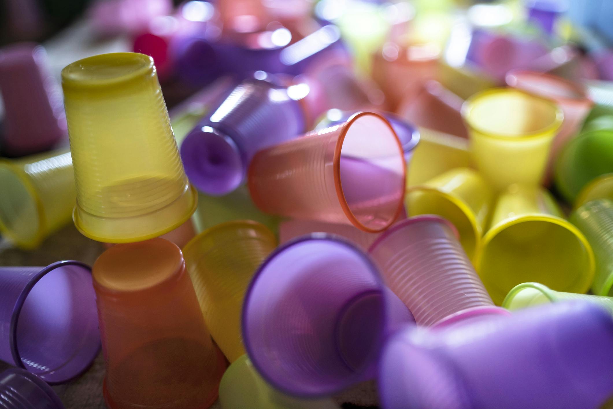 Een berg plastic bekertjes in de kleuren geel, paars en oranje.