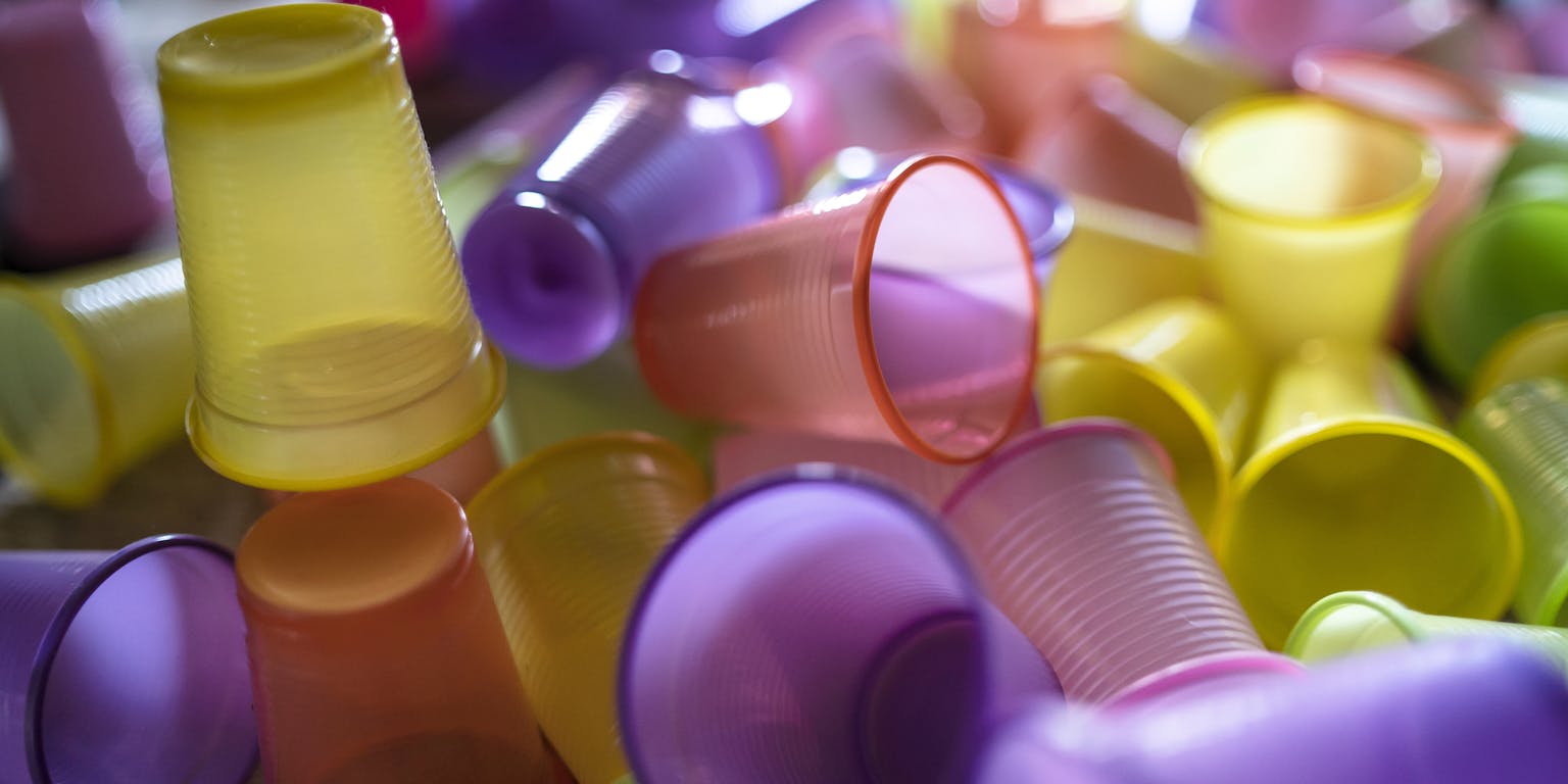 Een berg plastic bekertjes in de kleuren geel, paars en oranje.