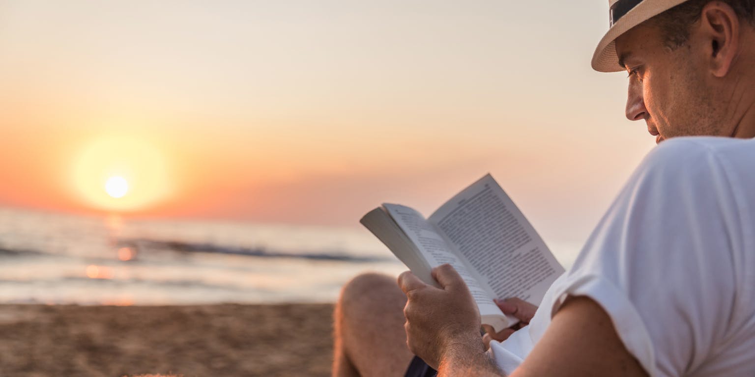 Een man die een boek leest op het strand.