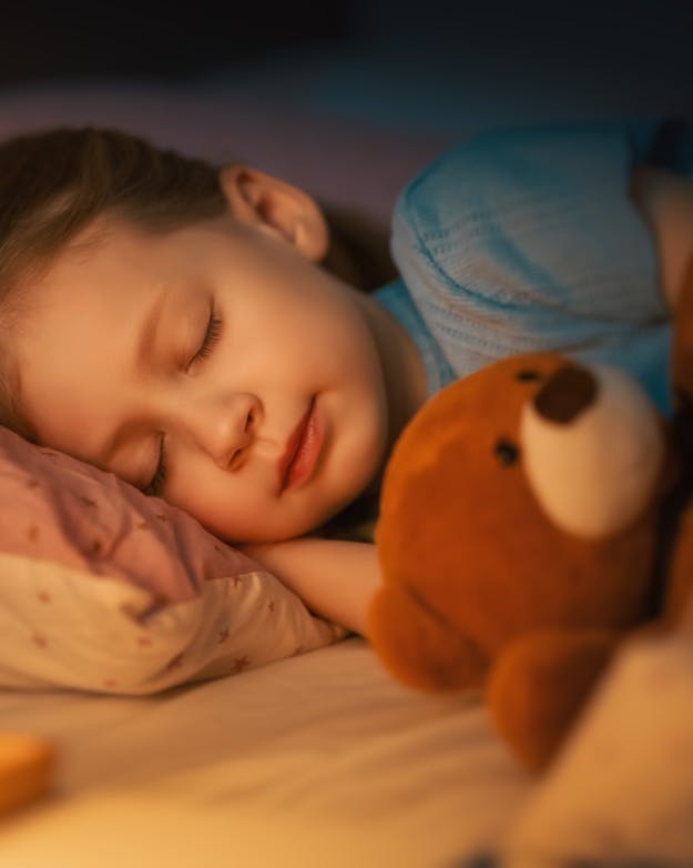 Maken nachtlampjes een kind bijziend? Het verband tussen de twee blijkt anders te liggen. Slapend meisje met een teddybeer en een lampje aan.