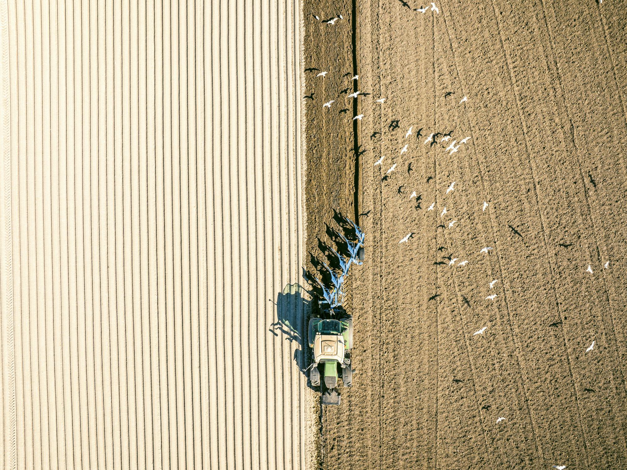 Een luchtfoto van een tractor die een veld ploegt.