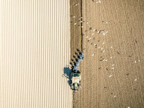 Een luchtfoto van een tractor die een veld ploegt.