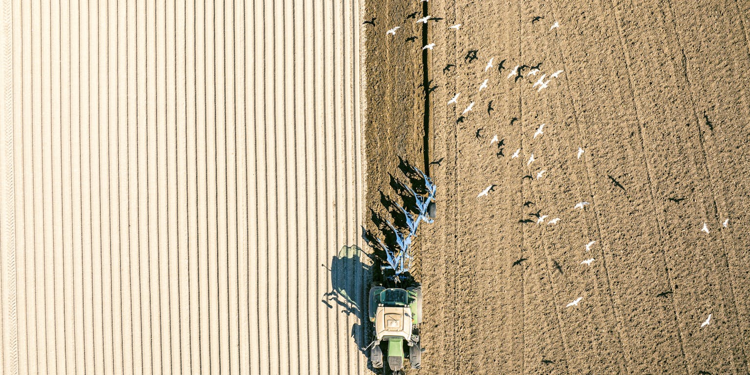 Een luchtfoto van een tractor die een veld ploegt.
