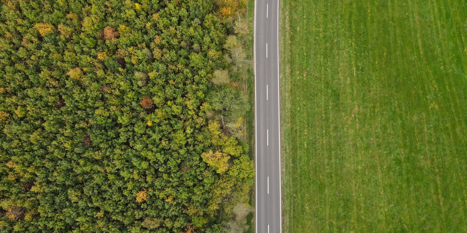 Een luchtfoto van een weg tussen het bos en een stuk land.