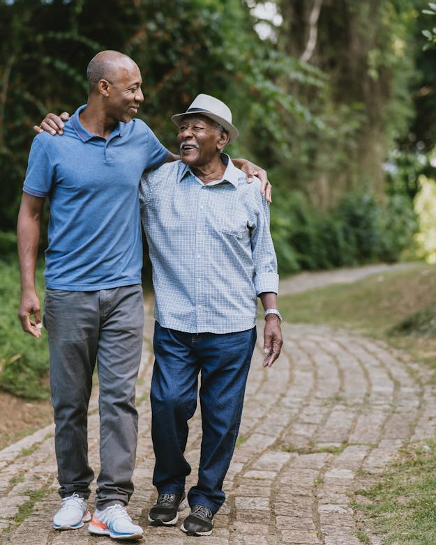 Oudere man en zijn volwassen zoon wandelen over een paadje, lachen naar elkaar Oudere man en zijn volwassen zoon wandelen over een paadje, lachen naar elkaar