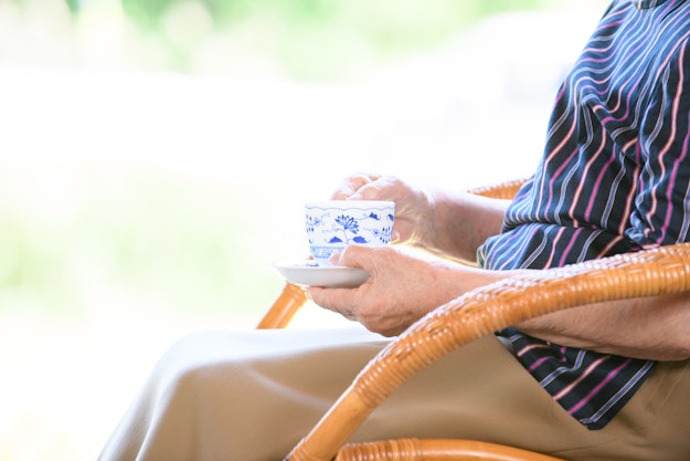 Zijaanzicht van een oudere vrouw met een kopje thee op een rieten stoel
