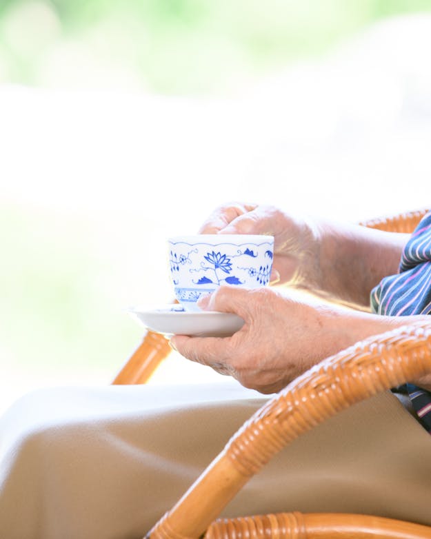 Zijaanzicht van een oudere vrouw met een kopje thee op een rieten stoel Zijaanzicht van een oudere vrouw met een kopje thee op een rieten stoel