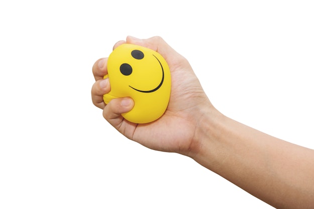 Hand die knijpt in een gele stressbal met een smiley erop.