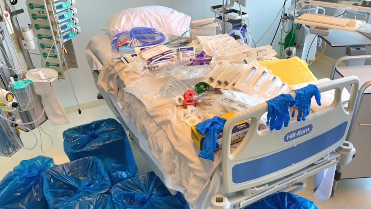 Een ziekenhuisbed ligt vol materialen: rubberen handschoenen, plastic jassen, absorberende bedmatjes, operatiemaskers, injectiespuiten etc.