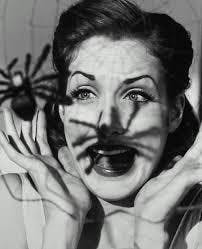 Zwart-witfoto van een vrouw met twee spinnen op haar gezicht.