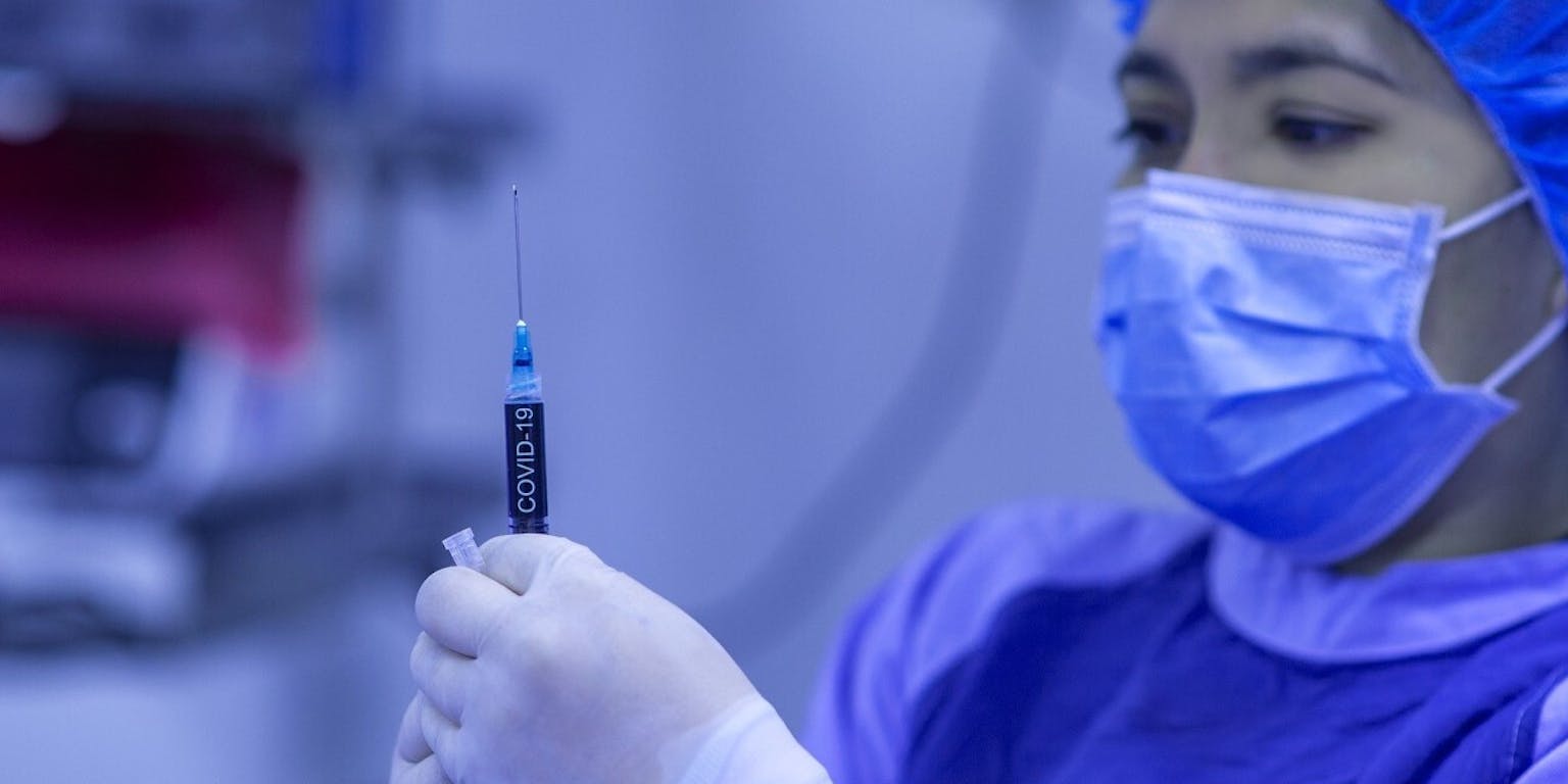Een chirurg met een mondkapje op die een corona injectiespuit vasthoudt.
