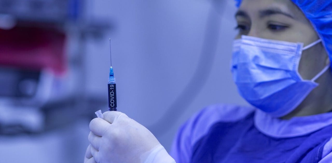 Een chirurg met een mondkapje op die een corona injectiespuit vasthoudt.