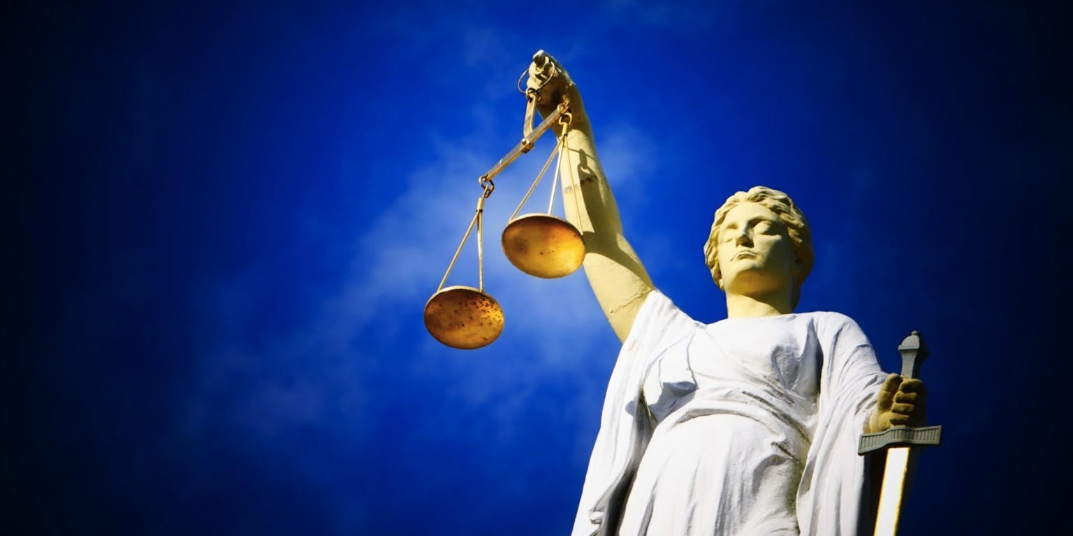 Een standbeeld van gerechtigheid met een weegschaal van gerechtigheid tegen een blauwe lucht.