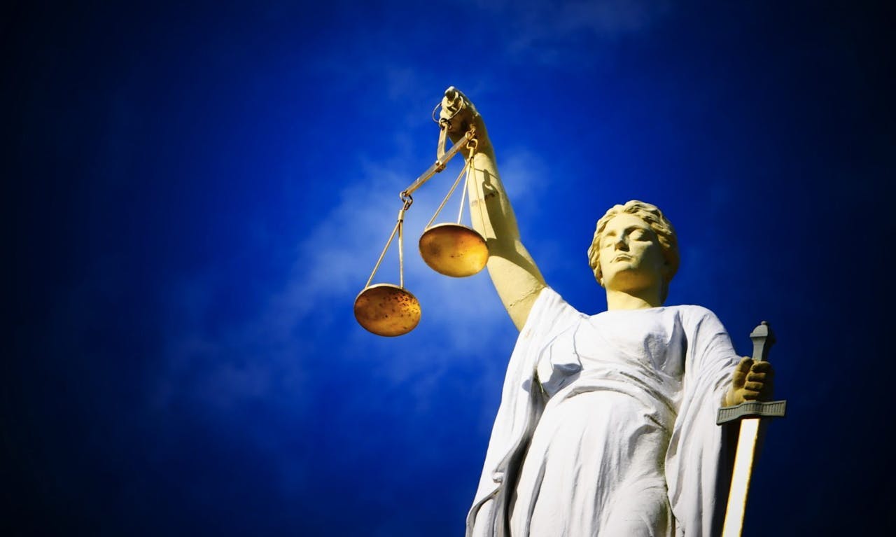 Een standbeeld van gerechtigheid met een weegschaal van gerechtigheid tegen een blauwe lucht.