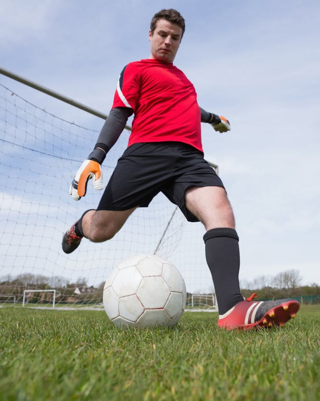 Sensoren die zijn verwerkt in voetbalshorts brengen de bewegingen van een speler in kaart. Keeper met rood shirt en zwarte short haalt uit om de witte voetbal weg te schoppen.