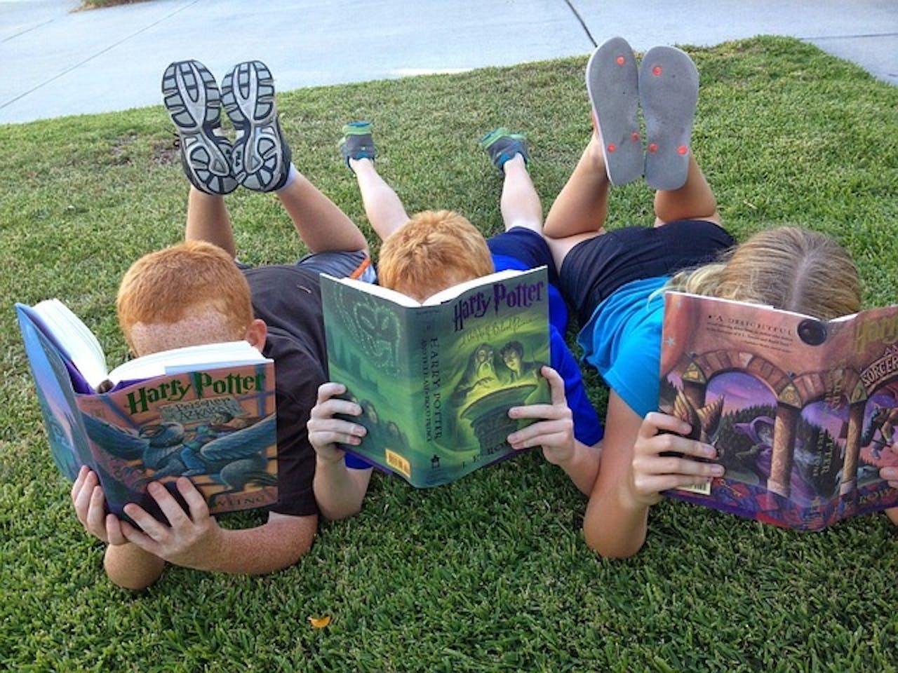 Drie kinderen liggen op het gras Harry Potter-boeken te lezen.