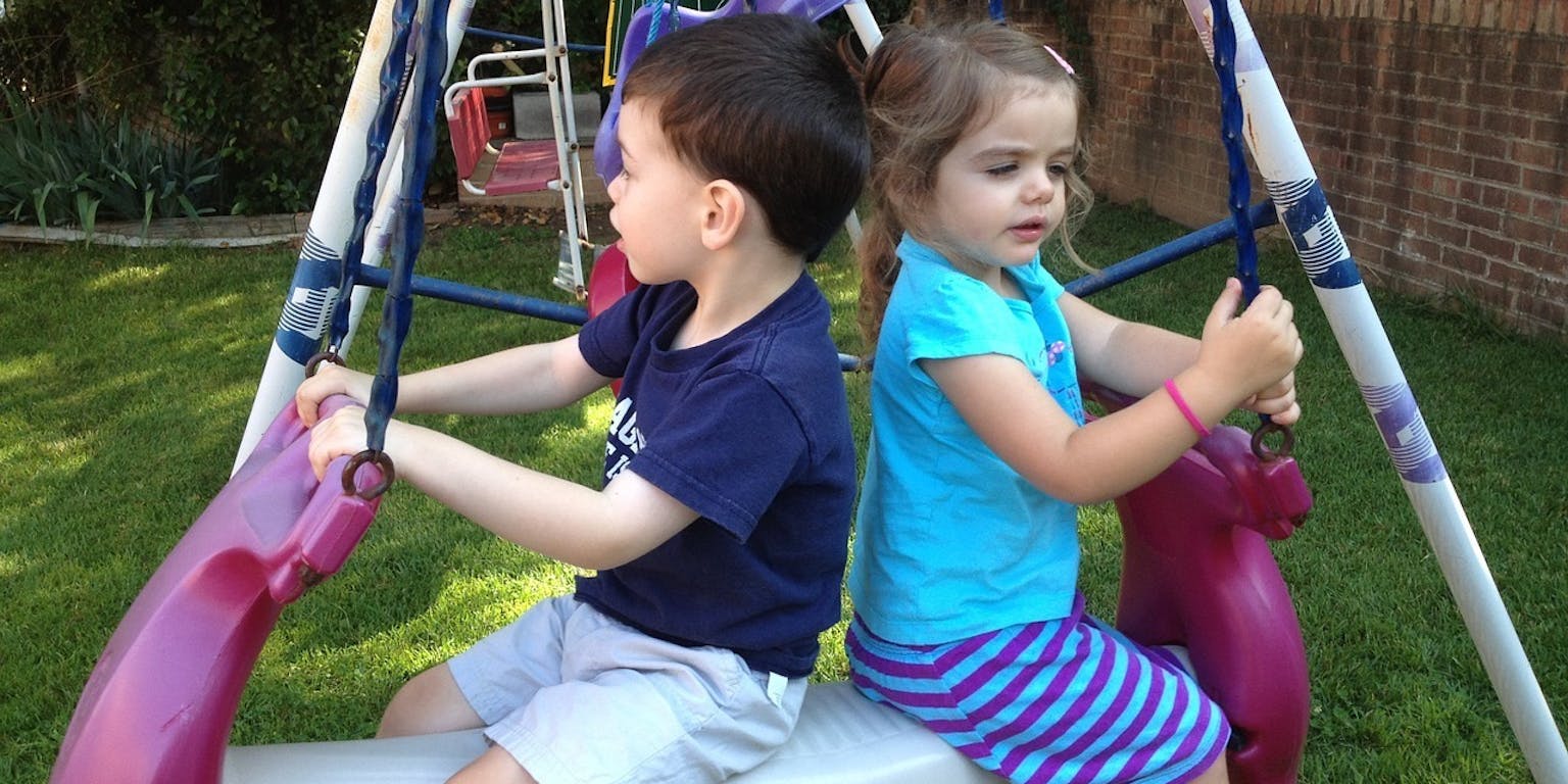 Twee kinderen zitten op een schommel in een achtertuin.