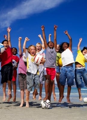 Een groep kinderen springt met voetballen op het strand.