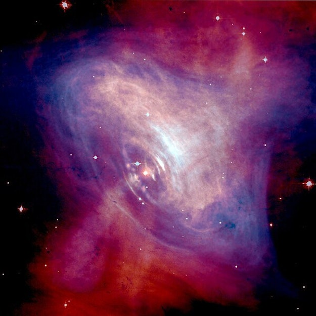 Een paars en rood gekleurde nevel tegen een zwarte sterrenhemel.