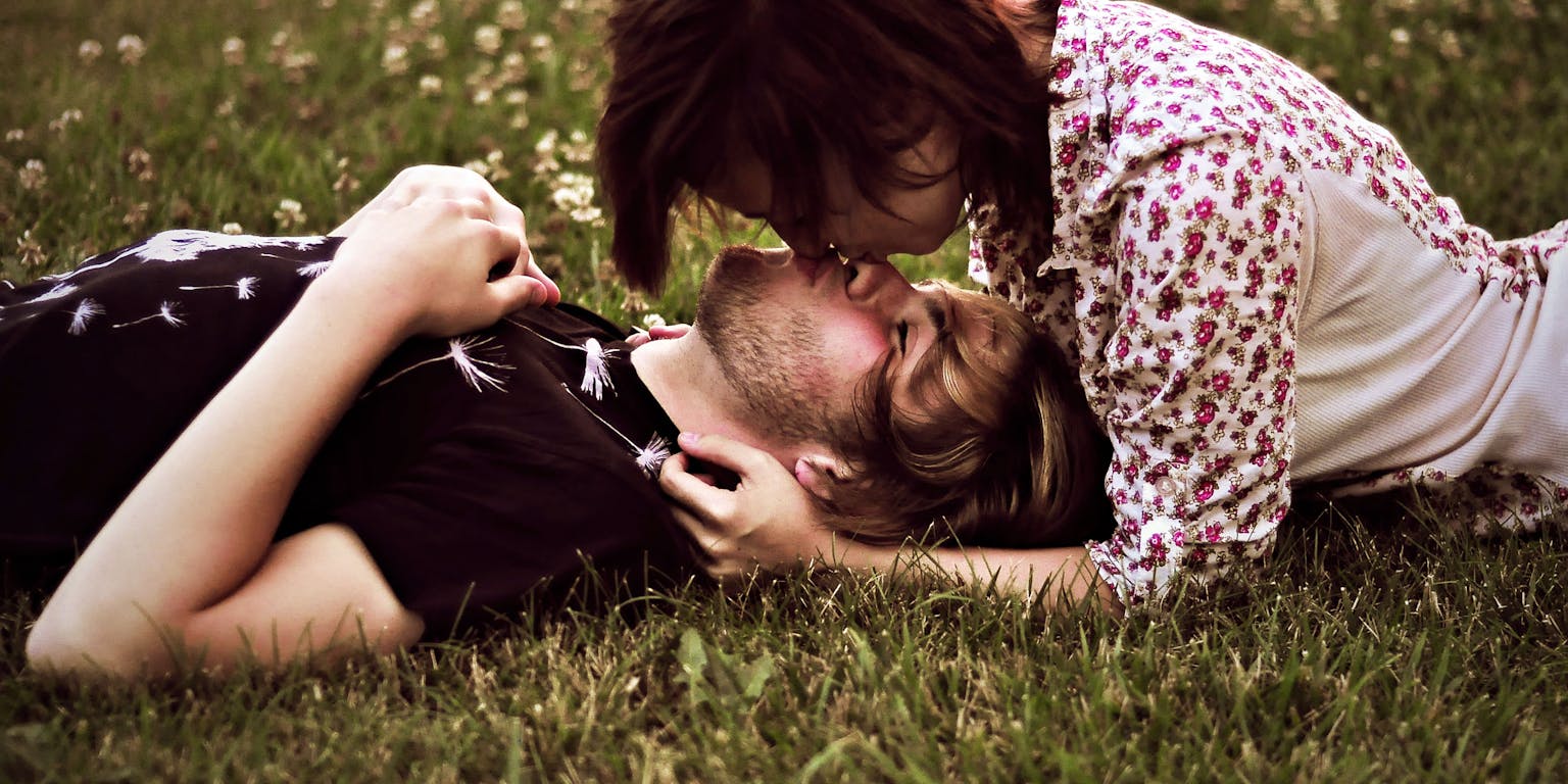 Een man en een vrouw liggen zoenend in het gras.