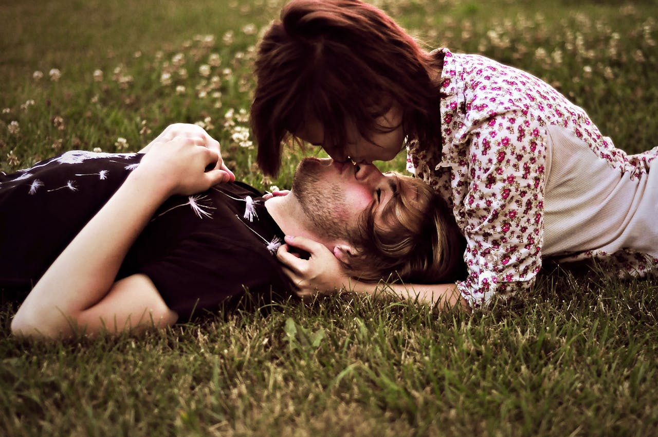 Een man en een vrouw liggen zoenend in het gras.