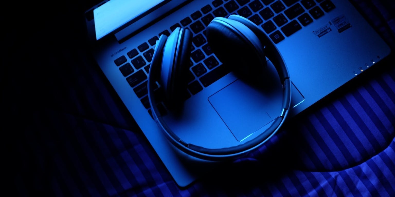 Een laptop op bed met een koptelefoon op. Over de afbeelding zit een blauwe filter.