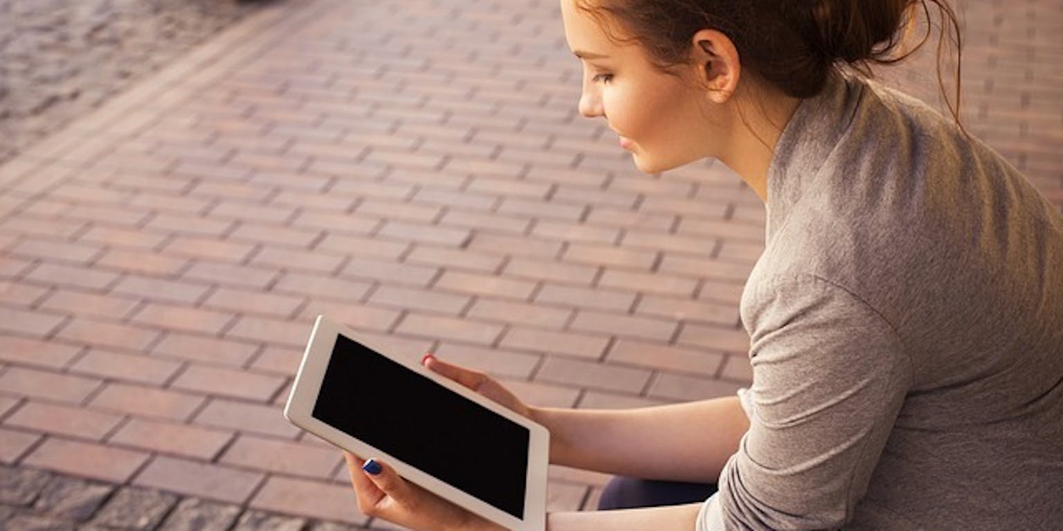 Een persoon zit op de stoep en leest vanaf een e-reader.