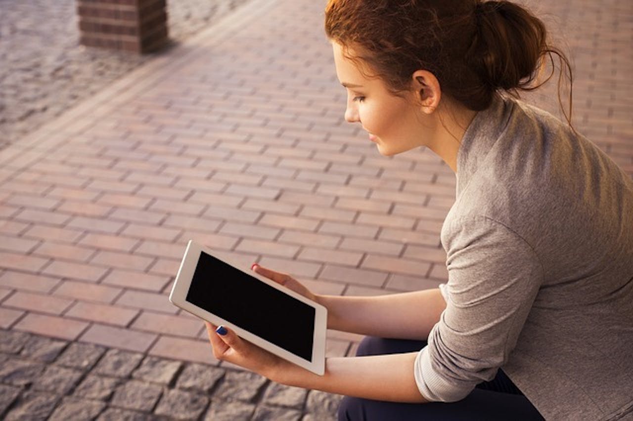 Een persoon zit op de stoep en leest vanaf een e-reader.