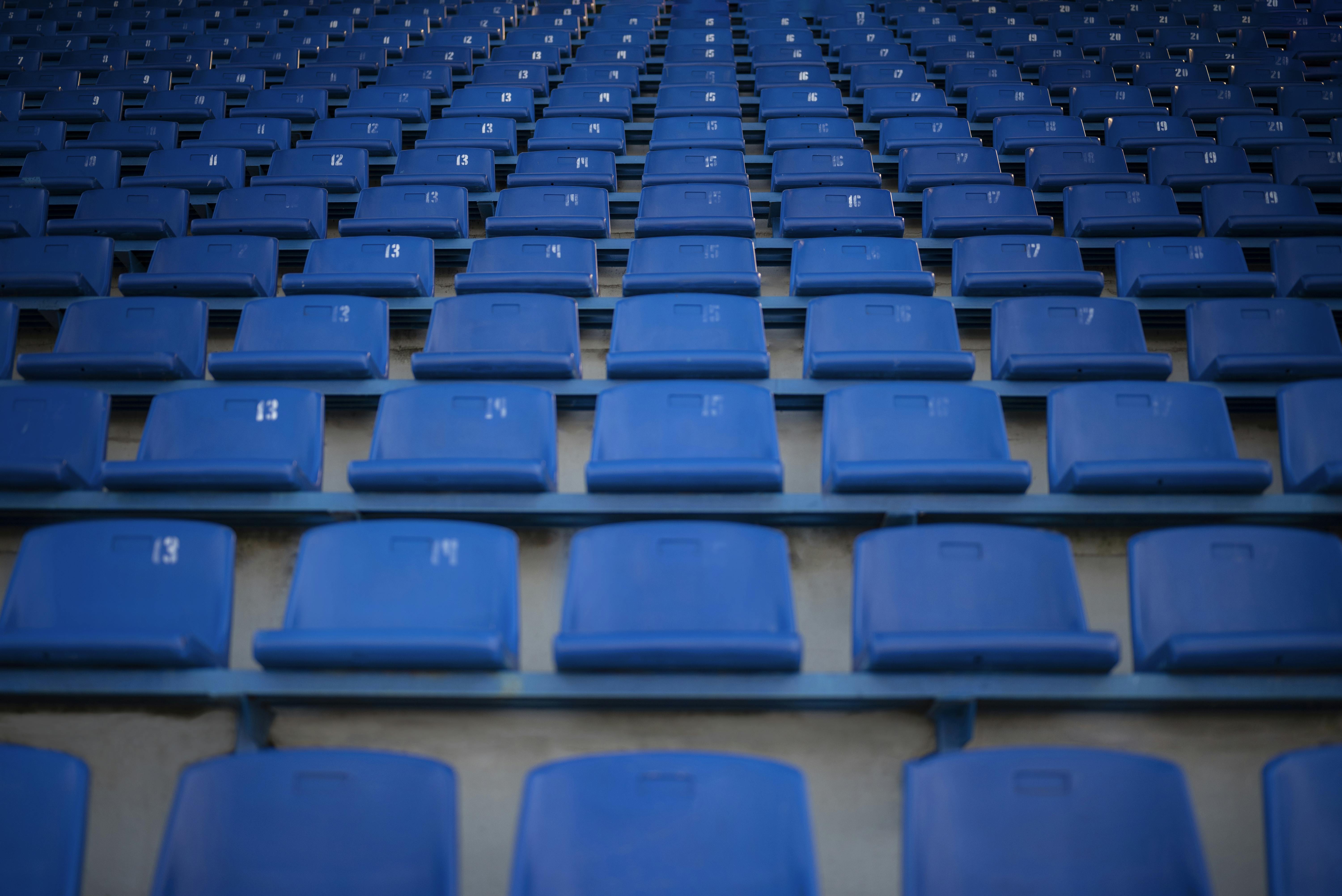 Rijen met blauwe plastic stoeltjes op een tribune.