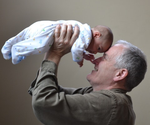 Oudere man houdt baby in de lucht, de voorhoofden raken elkaar