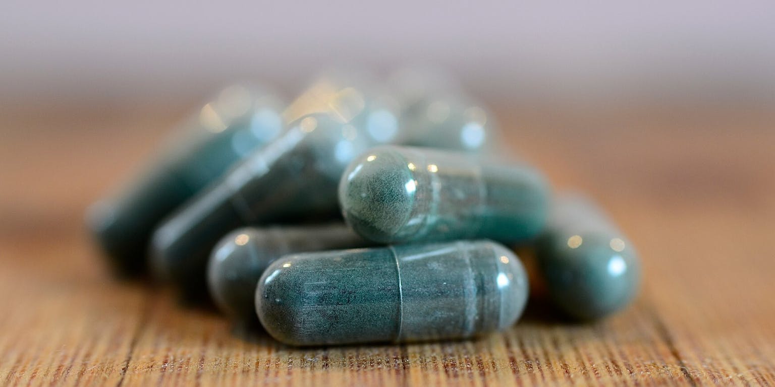 Een stapel groene pillen op een houten tafel.