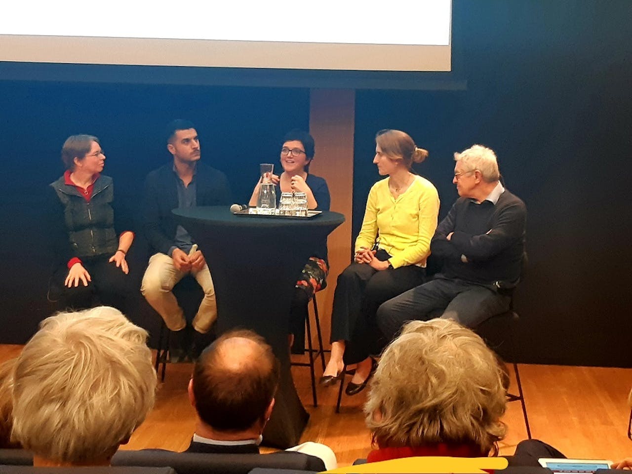 Vijf sprekers op een podium. Mirjam Ernestus, Khalid Mourigh, Sharon Unsworth, Merel Keijzer en Roeland van Hout.