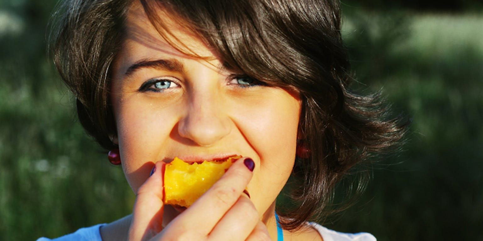 Een kind eet een stuk fruit.