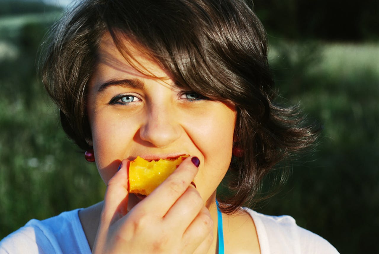 Een kind eet een stuk fruit.