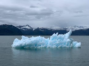 Een ijsberg die in het water drijft met bergen op de achtergrond.