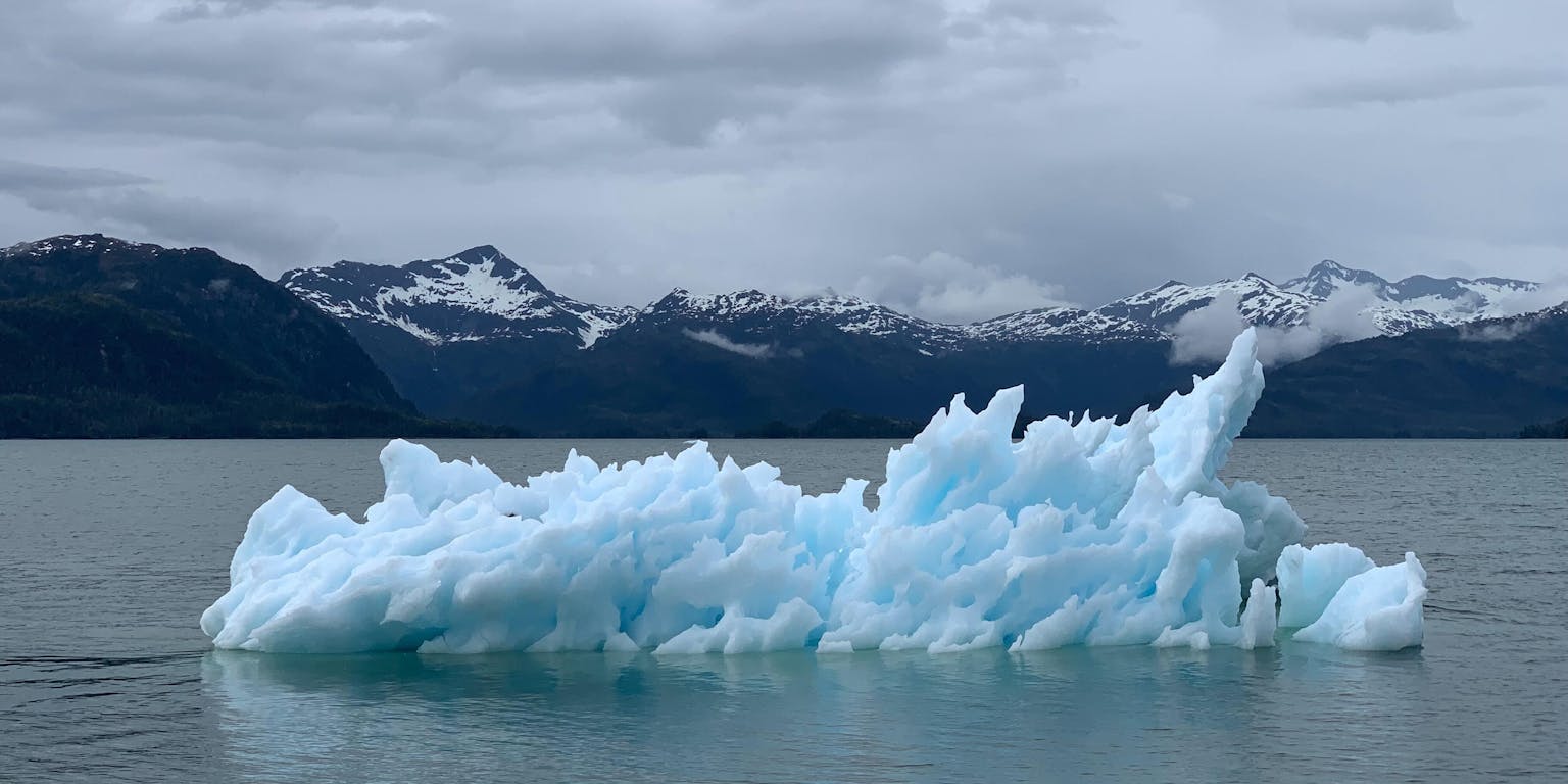 Een ijsberg die in het water drijft met bergen op de achtergrond.