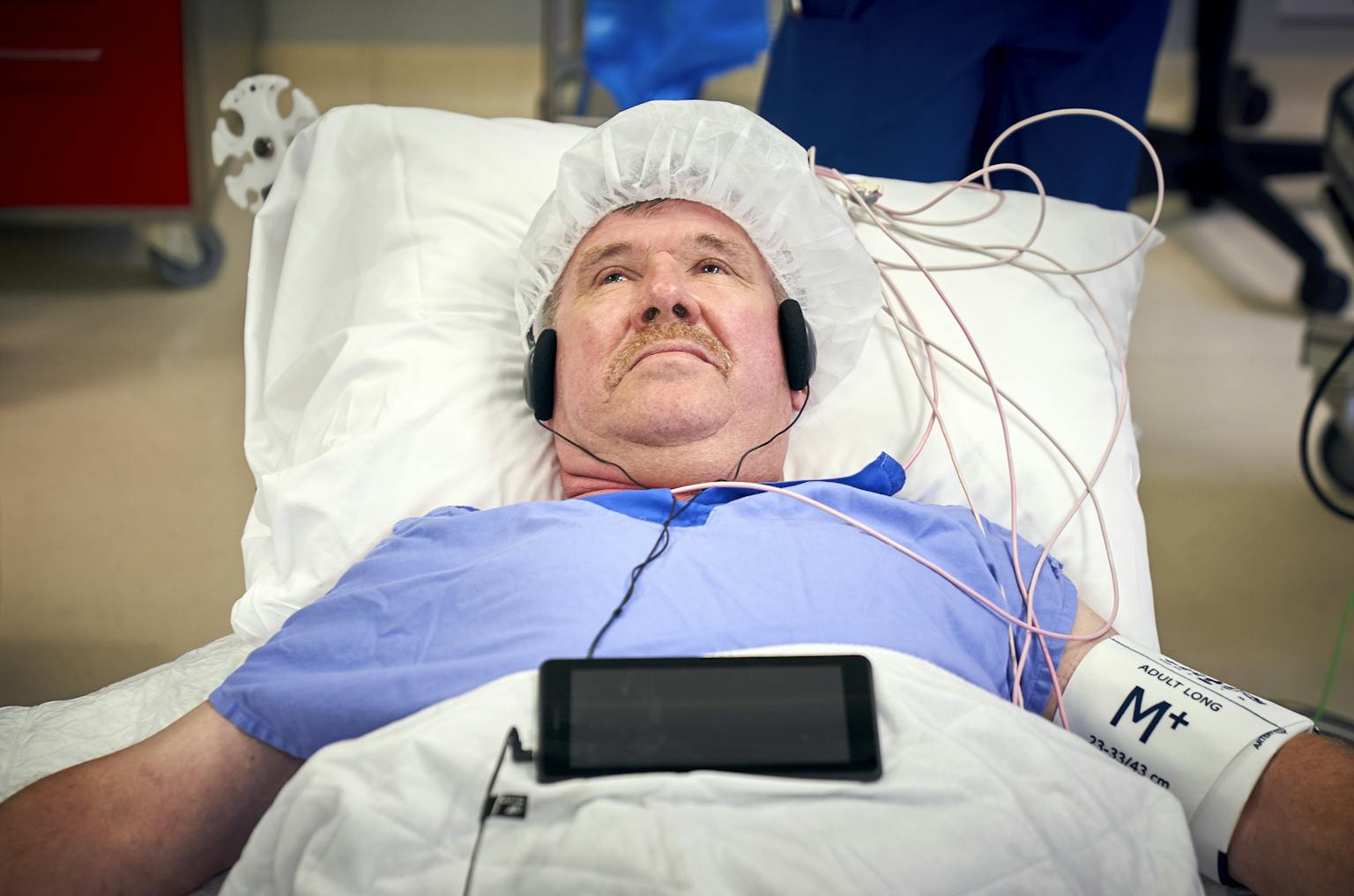 Een man ligt in een ziekenhuisbed met een koptelefoon op.