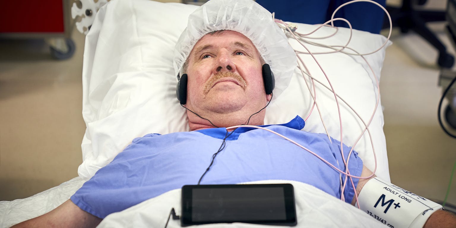Een man ligt in een ziekenhuisbed met een koptelefoon op.