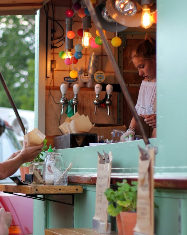 Vrouw serveert eten vanuit een lichtblauwe versierde foodtruck. Vrouw serveert eten vanuit een lichtblauwe versierde foodtruck.