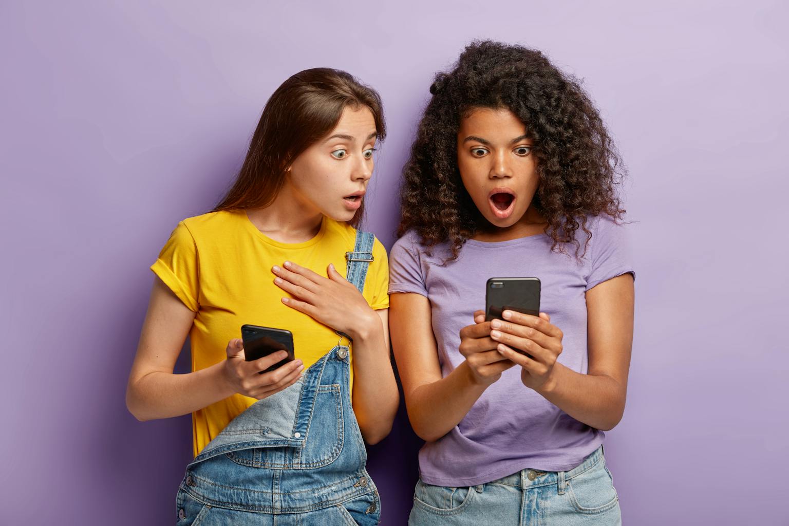 twee jonge vrouwen kijken verbaasd en geshockeerd naar berichten op hun telefoon van social media