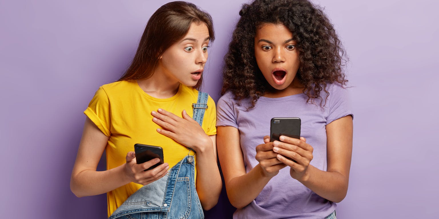 twee jonge vrouwen kijken verbaasd en geshockeerd naar berichten op hun telefoon van social media
