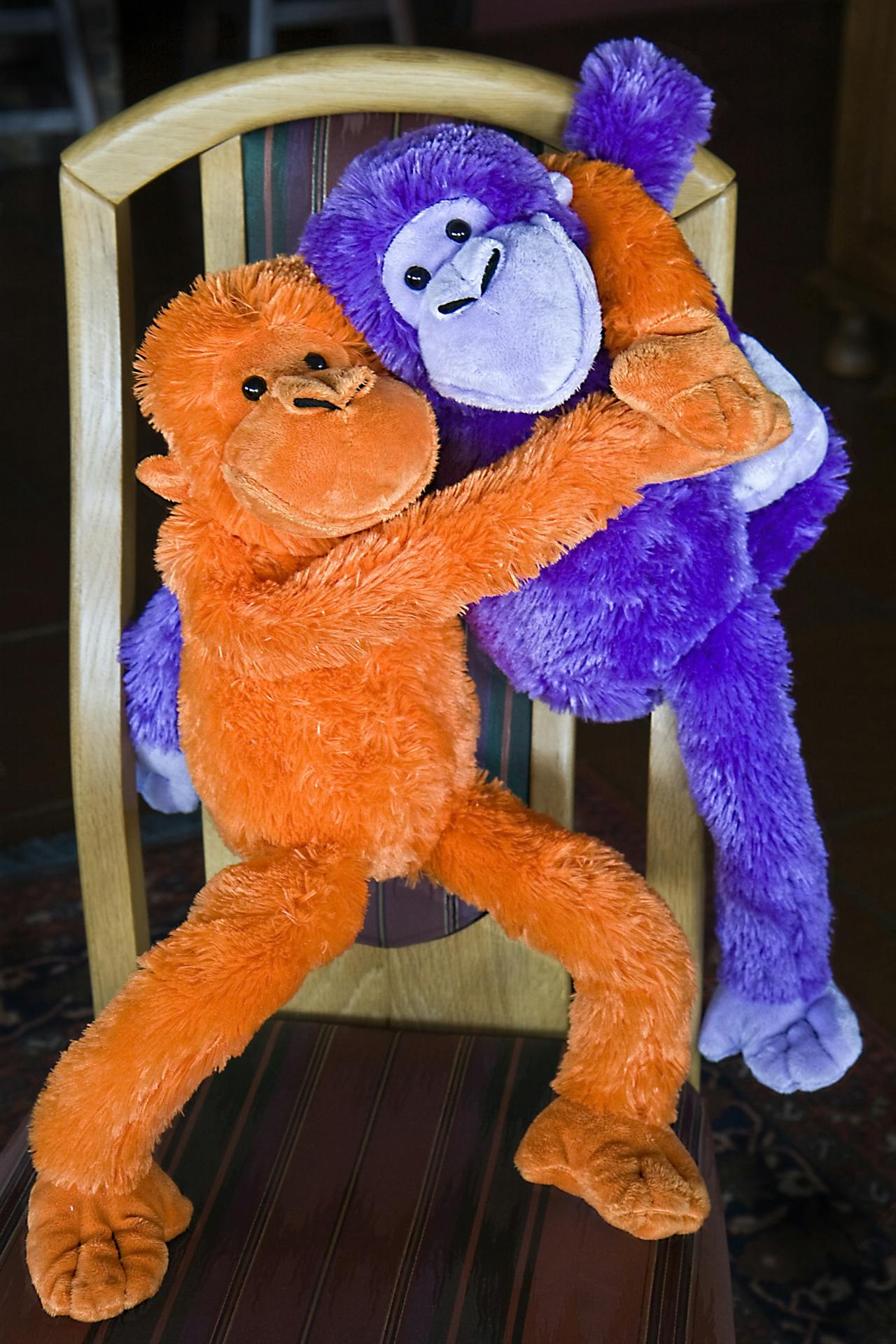 Een oranje en een paarse knuffelaap zitten op een houten stoeltje.