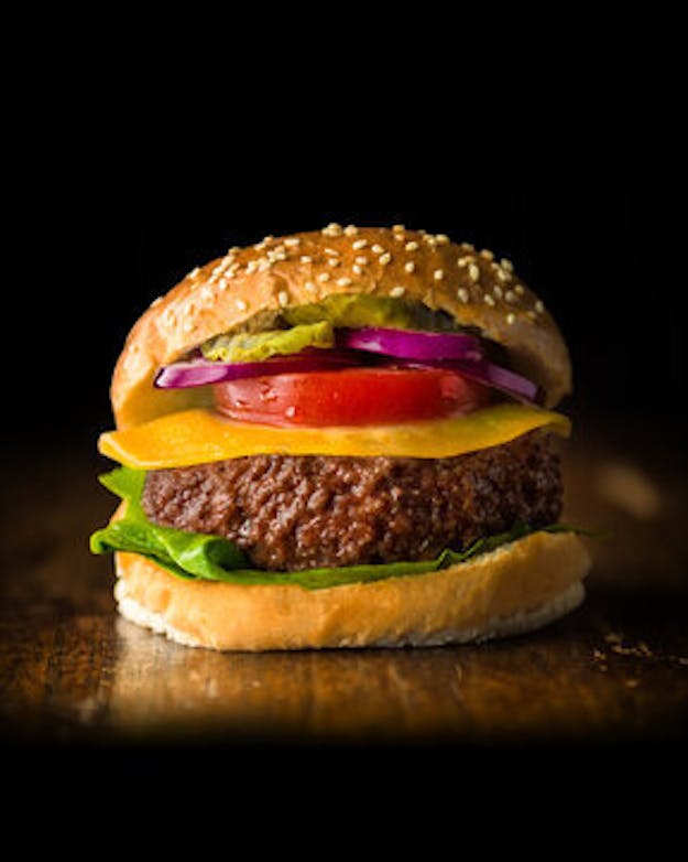 Om uit te zoeken of een runderburger van kweekvlees duurzamer is dan een runderburger van gewone koeien, moet je voor beiden helemaal terug in de keten hoe ze gemaakt zijn. Dus tot aan de kunstmest die het gras helpt groeien en de aminozuren die nodig zijn voor het groeimedium. Foto van een broodje hamburger met een donkere achtergrond. De hamburger is van kweekvlees