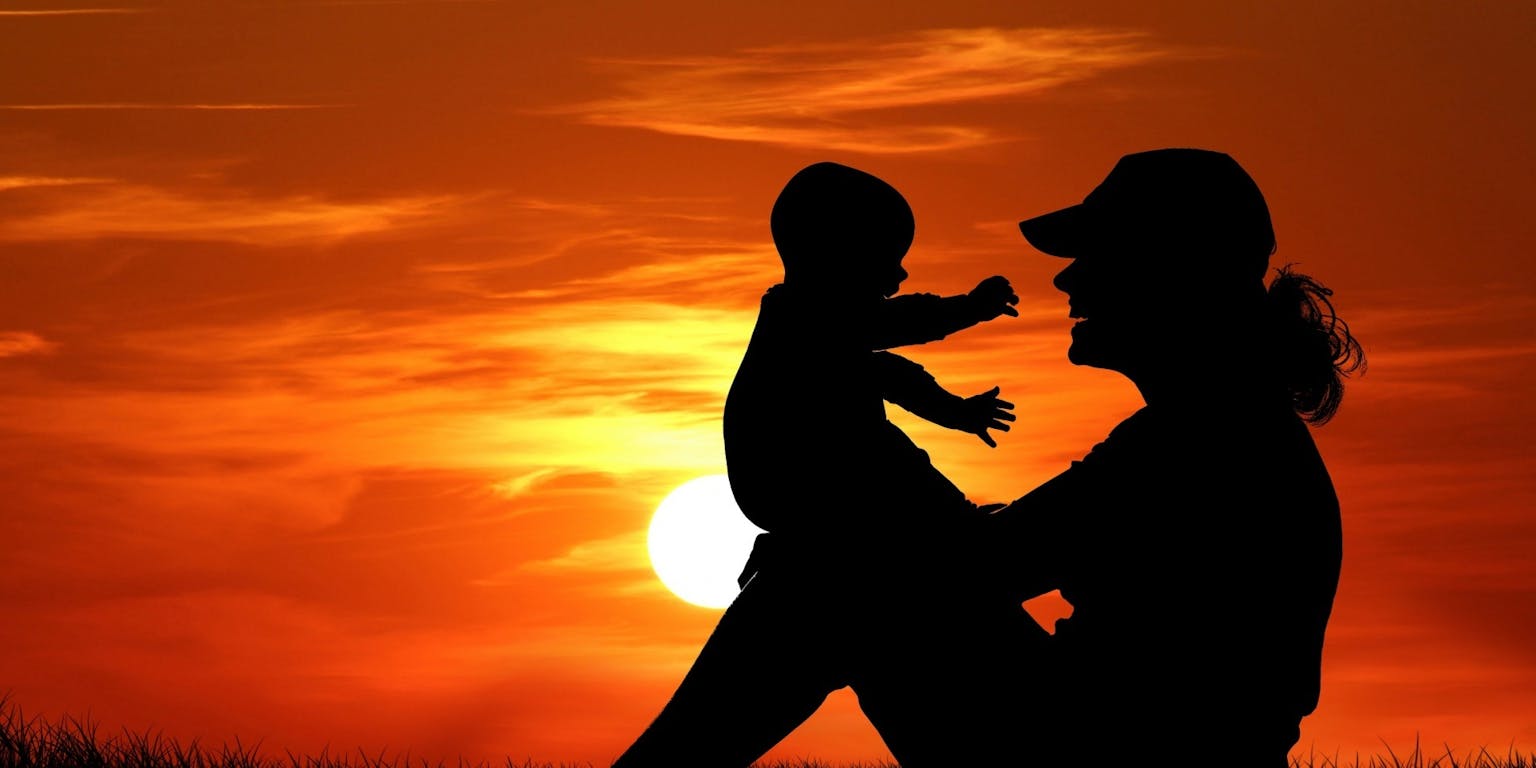 Een silhouet van een vrouw die een kind vasthoudt bij zonsondergang.