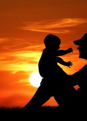 Een silhouet van een vrouw die een kind vasthoudt bij zonsondergang.