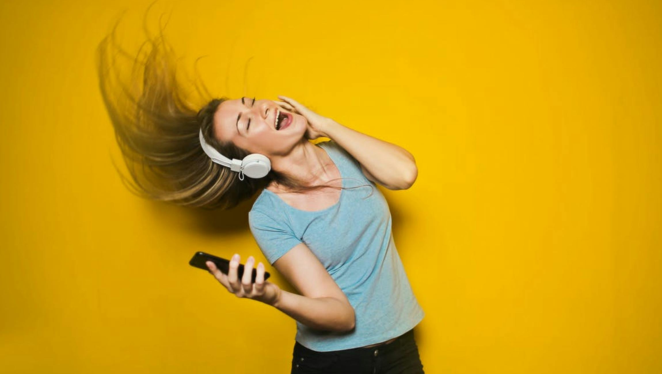 Een jonge vrouw die een koptelefoon draagt en naar muziek luistert op een gele achtergrond.
